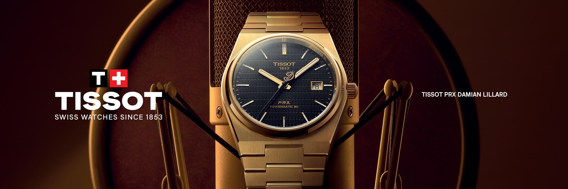 Eine goldene Tissot PRX-Uhr mit blauem Zifferblatt steht aufrecht in der Auslage. Das Tissot-Logo und "Swiss watches since 1853" erscheinen auf der linken Seite, während "Tissot PRX Damian Lillard" auf der rechten Seite zu sehen ist.