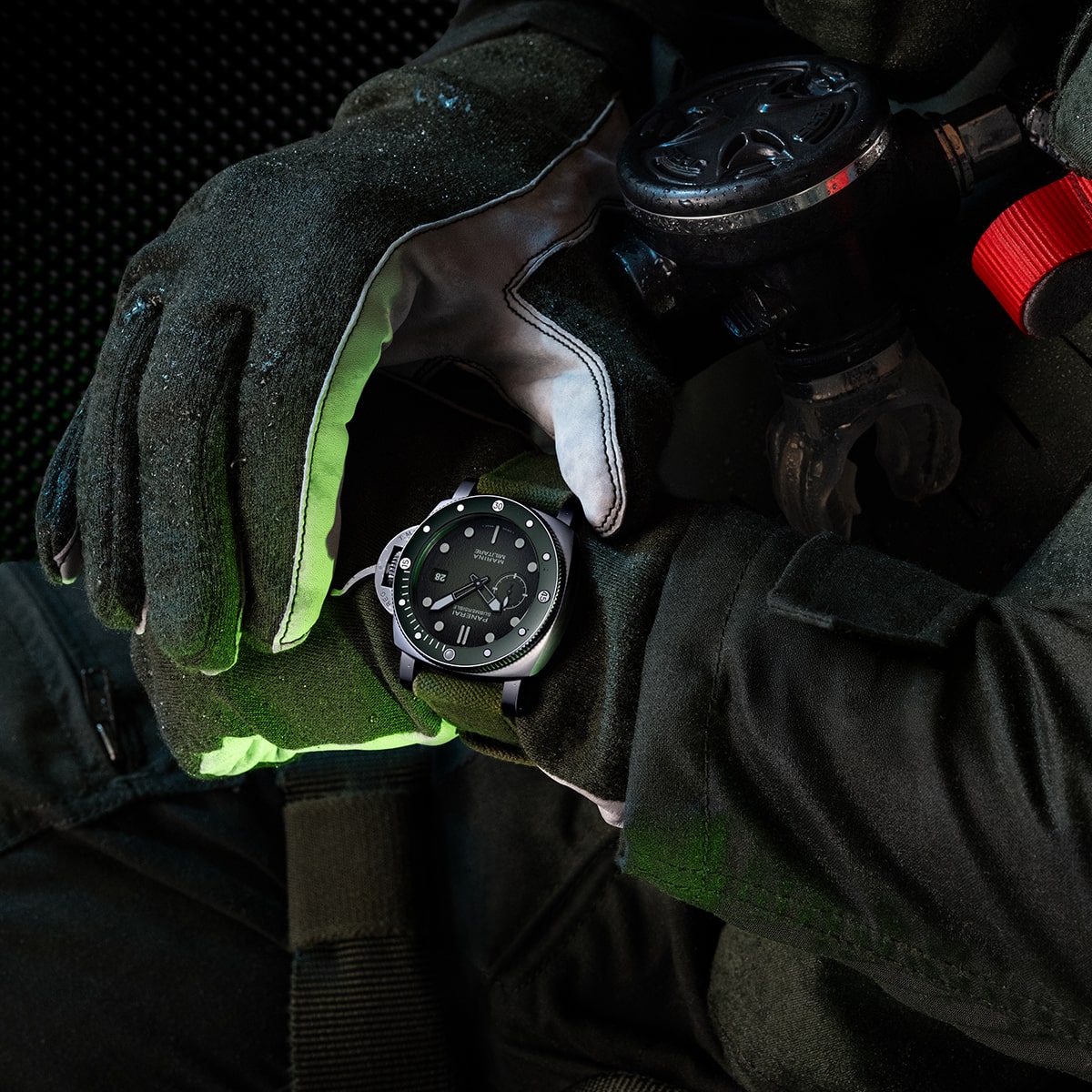 Eine Person mit dunklen Handschuhen und schwarzem Anzug überprüft eine Panerai Submersible Armbanduhr an ihrem linken Handgelenk, während sie ein Atemgerät in der Hand hält, was auf ein professionelles oder taktisches Umfeld hindeutet.